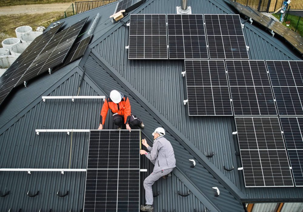 Workers measuring photovoltaic solar panels with tape measure. Men taking measurements before mounting solar module on roof of house for generating electricity through photovoltaic effect. Aerial view